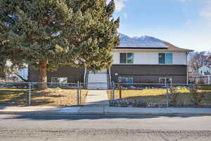 View of front of property with brick siding, a fenced front yard, a mountain view, roof mounted solar panels, and a gate