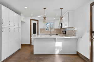Kitchen featuring white cabinets, a kitchen breakfast bar, decorative backsplash, a peninsula, and hanging light fixtures