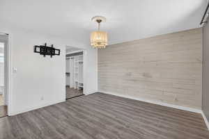 Unfurnished dining area with wooden walls, wood finished floors, and hanging lights