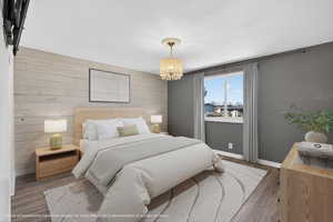 Bedroom with an accent wall, wood walls, wood finished floors, and suspended lighting