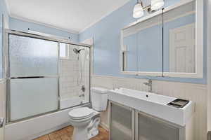 Bathroom featuring bath / shower combo with glass door, a wainscoted wall, vanity, ornamental molding, and light tile patterned floors