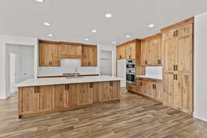 Kitchen featuring a center island with sink, wood tiled floors, recessed lighting, light stone counters, and stainless steel appliances