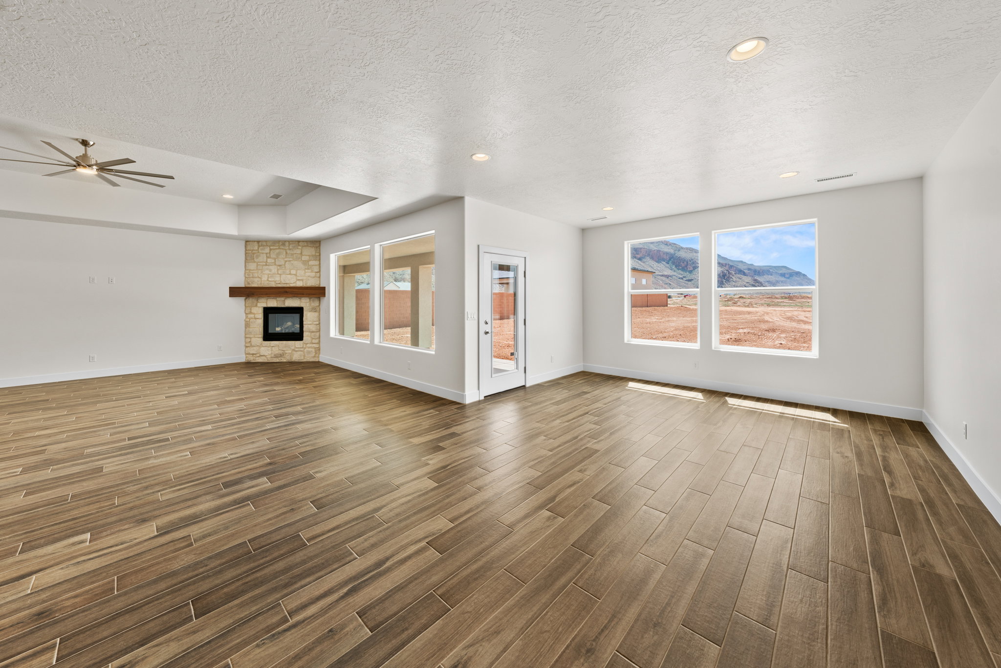 Unfurnished living room with a fireplace, wood finish floors, a ceiling fan, recessed lighting, and a textured ceiling