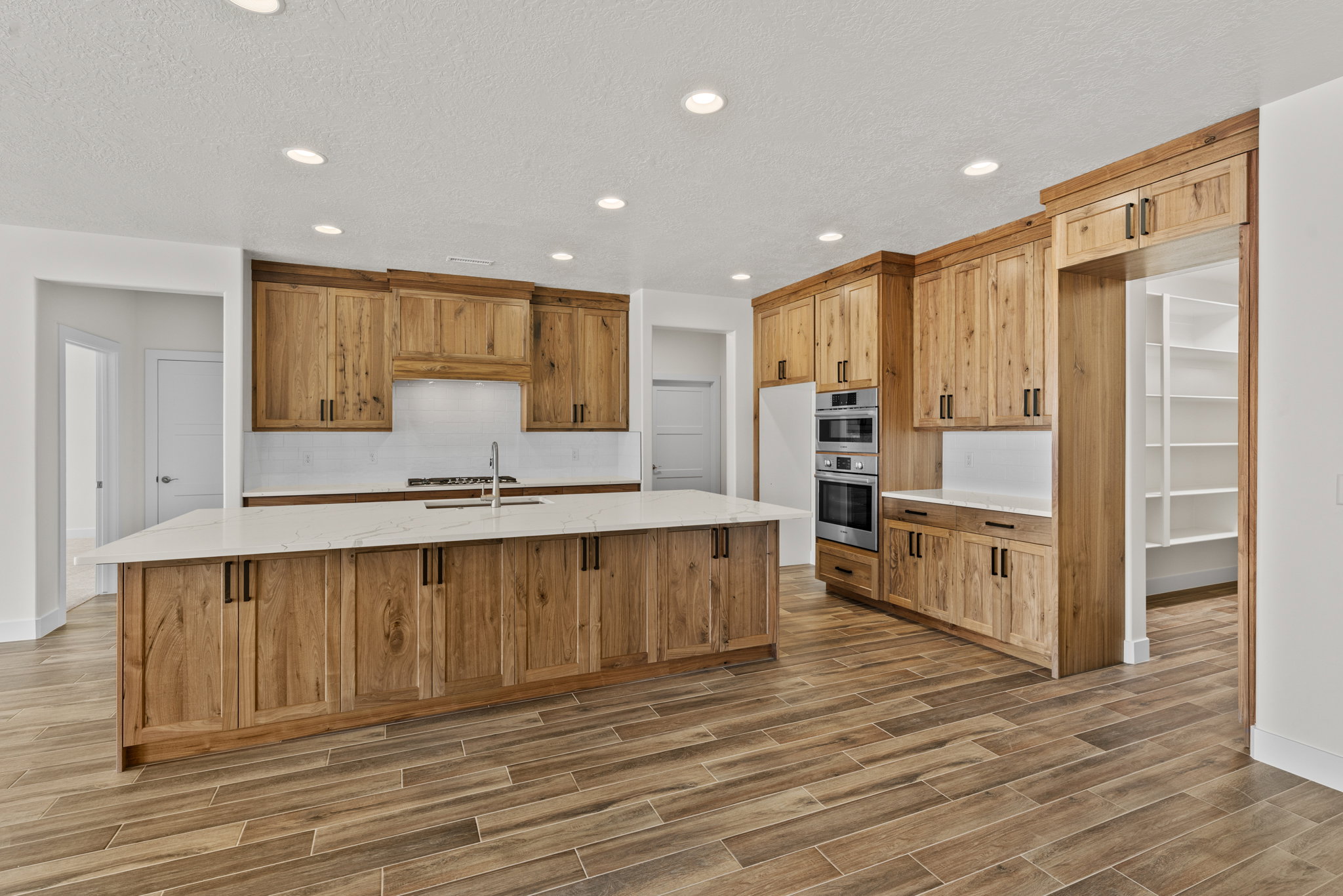 Kitchen featuring light stone countertops, wood finish floors, recessed lighting, an island with sink, and wood finish cabinetry