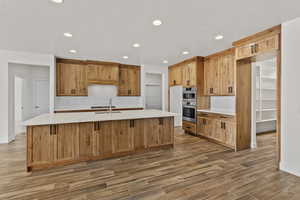 Kitchen featuring light stone countertops, wood finish floors, recessed lighting, an island with sink, and wood finish cabinetry