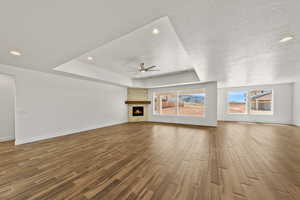 Unfurnished living room featuring a raised ceiling, a stone fireplace, wood tiled floors, recessed lighting, and ceiling fan