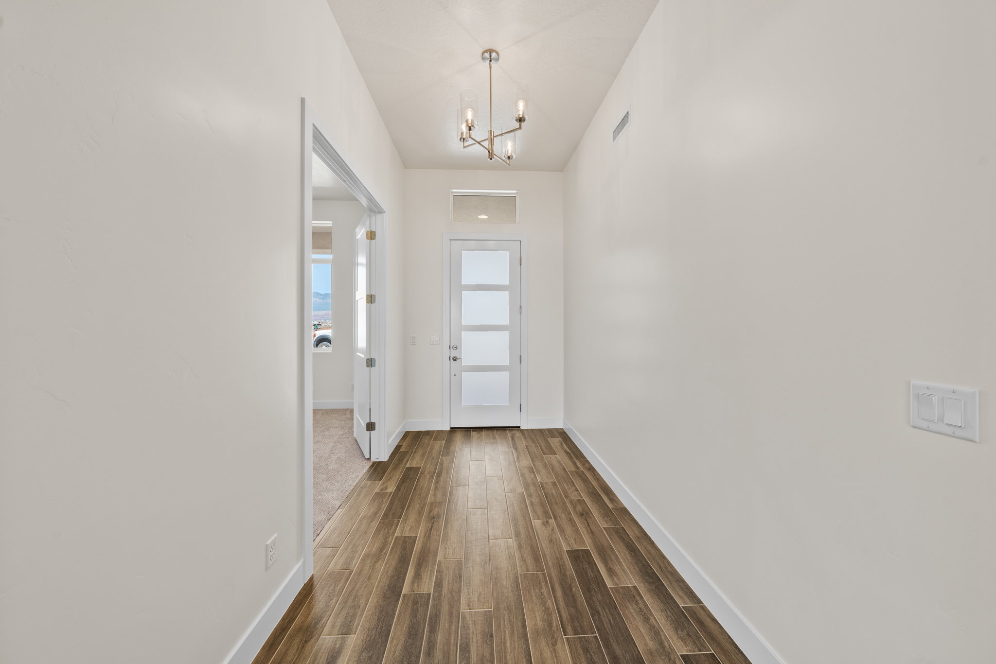 Doorway with wood finished floors and suspended lighting