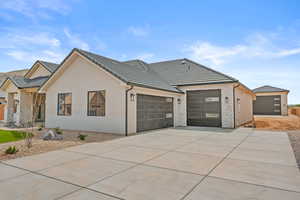 View of front of property with concrete driveway, a tile roof, an attached garage, stucco siding, and stone siding