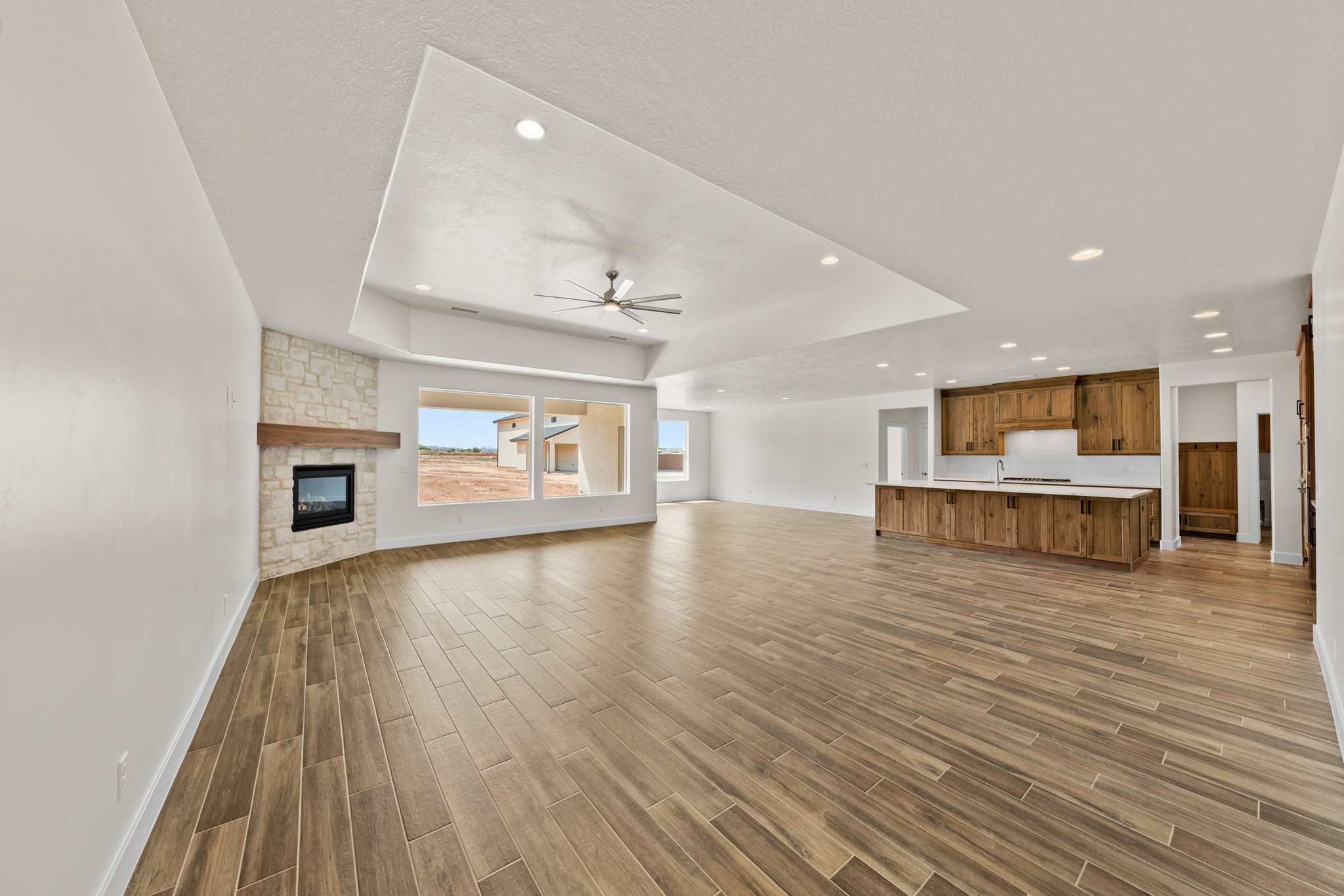 Unfurnished living room with a fireplace, wood finish floors, a ceiling fan, a tray ceiling, and recessed lighting