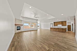 Unfurnished living room with a fireplace, wood finish floors, a ceiling fan, a tray ceiling, and recessed lighting