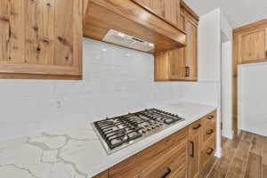 Kitchen featuring tasteful backsplash, stainless steel gas stovetop, wood tiled floors, and light stone countertops