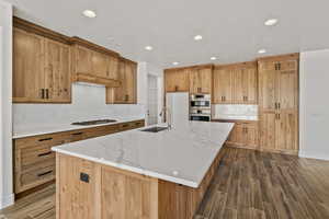 Kitchen featuring wood tiled floors, a kitchen island with sink, backsplash, light stone counters, and recessed lighting