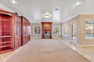 Unfurnished living room with light colored carpet, a fireplace, and crown molding