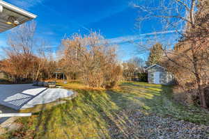 View of grassy yard featuring a storage unit and a patio
