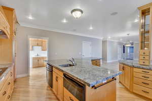 Kitchen featuring crown molding, a warming drawer, a kitchen island with sink, light wood finish cabinets, and light wood finished floors
