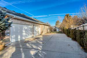 View of side of home featuring driveway, brick siding, an outdoor structure, and an attached garage