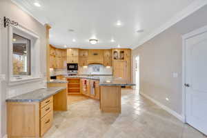 Kitchen with crown molding, light wood finish cabinets, an island with sink, a kitchen bar, and decorative backsplash