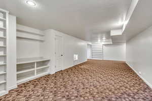 Finished basement with a textured ceiling, built in shelves, and carpet