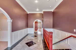 Hallway with arched walkways, crown molding, wainscoting, and a decorative wall