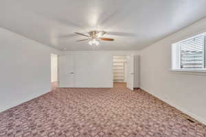 Unfurnished bedroom featuring a walk in closet, carpet floors, and a ceiling fan