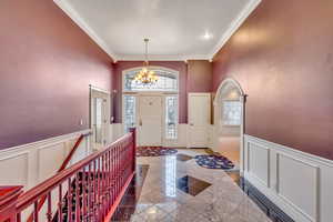 Foyer entrance featuring arched walkways, a decorative wall, wainscoting, ornamental molding, and a chandelier