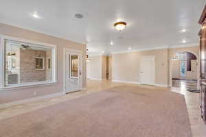 Unfurnished living room with arched walkways, light colored carpet, recessed lighting, and crown molding