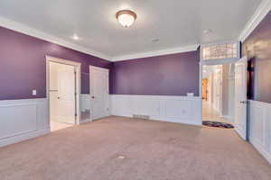 Unfurnished bedroom with a decorative wall, a wainscoted wall, ornamental molding, and light carpet