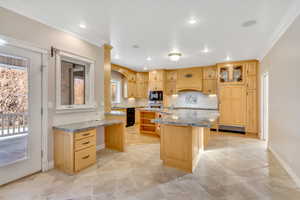 Kitchen featuring light wood finish cabinets, crown molding, light stone counters, glass insert cabinets, and light tile patterned floors