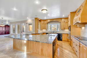 Kitchen with light wood finish cabinets, a large island with sink, light stone countertops, black appliances, and recessed lighting