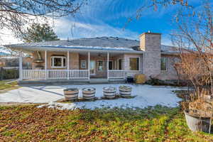 Rear view of house featuring a chimney, brick siding, a porch, and a patio