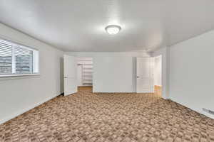 Unfurnished bedroom with a walk in closet, carpet flooring, and a textured ceiling