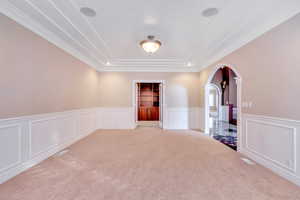 Empty room with arched walkways, wainscoting, a decorative wall, and carpet flooring