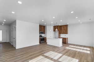 Kitchen with open floor plan, a kitchen island with sink, stainless steel appliances, light wood-style flooring, and recessed lighting