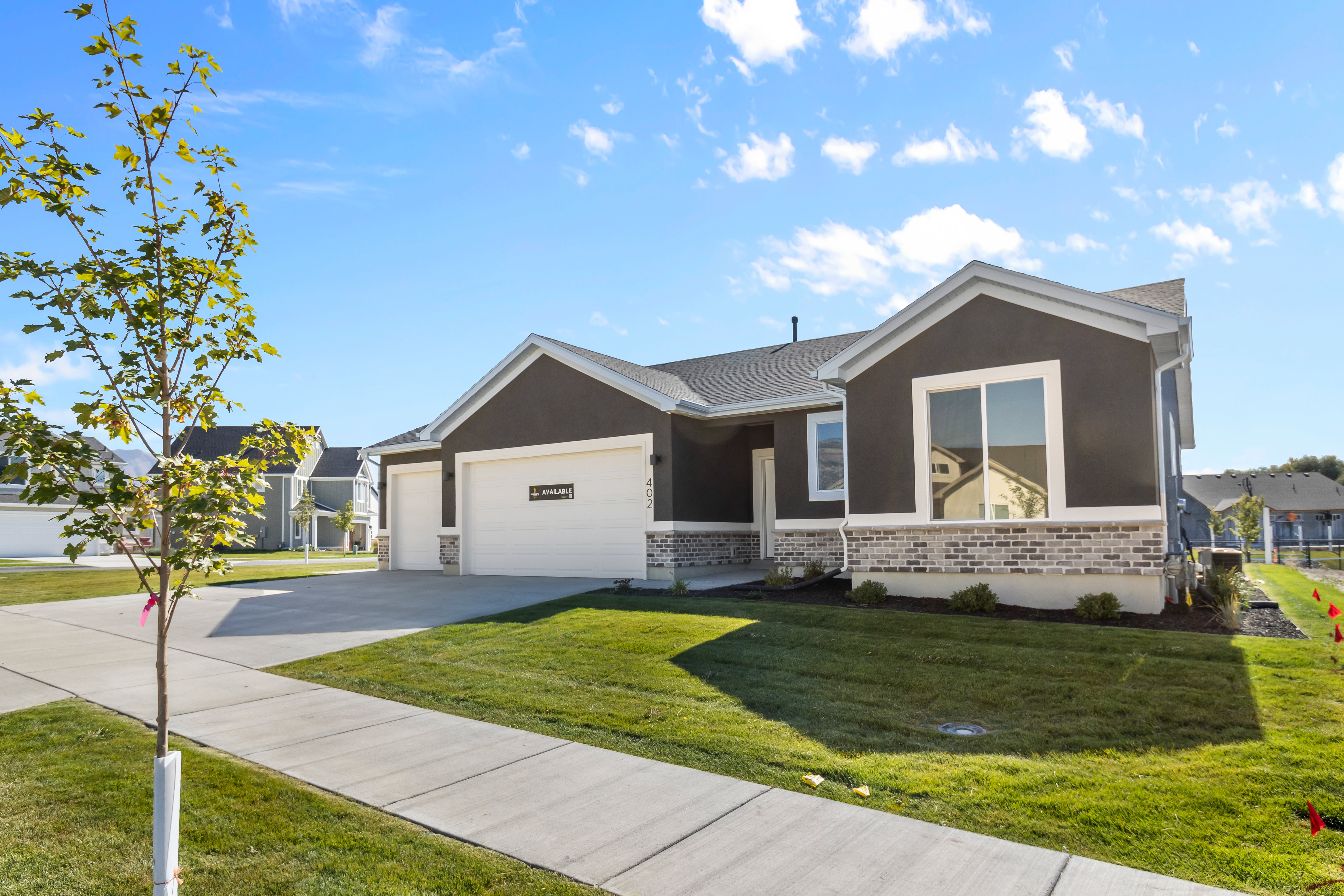 Ranch-style home featuring a front lawn, driveway, stucco siding, a garage, and brick siding