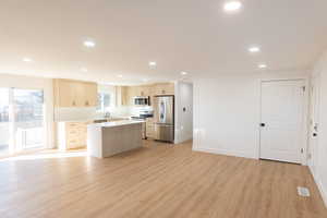 Kitchen featuring light wood finish cabinets, a center island, stainless steel appliances, recessed lighting, and open floor plan