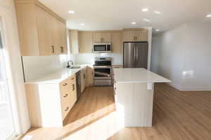 Kitchen featuring light wood finish cabinetry, stainless steel appliances, recessed lighting, light stone counters, and a center island