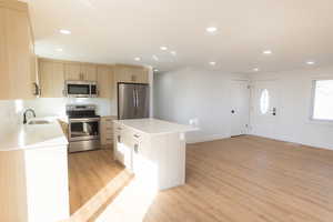 Kitchen featuring stainless steel appliances, recessed lighting, light wood finish cabinetry, light wood-style flooring, and a kitchen island