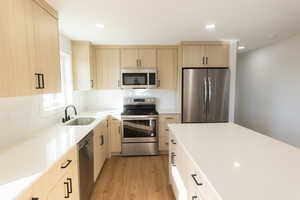 Kitchen with light wood finish cabinets, stainless steel appliances, light wood-style flooring, recessed lighting, and light stone counters