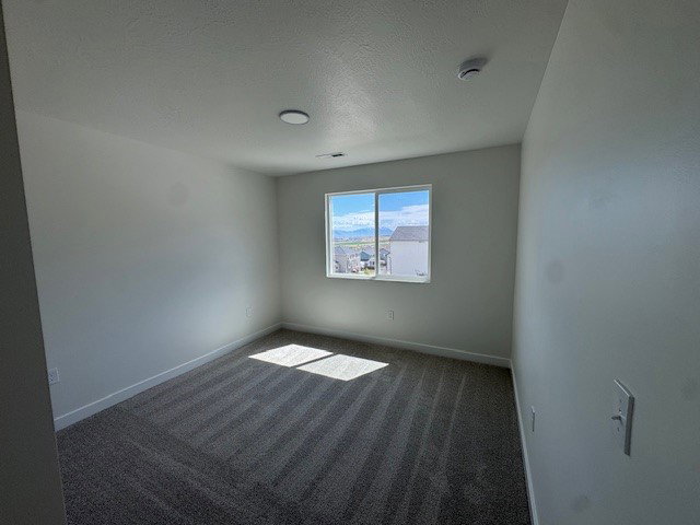 Unfurnished room with dark carpet and a textured ceiling