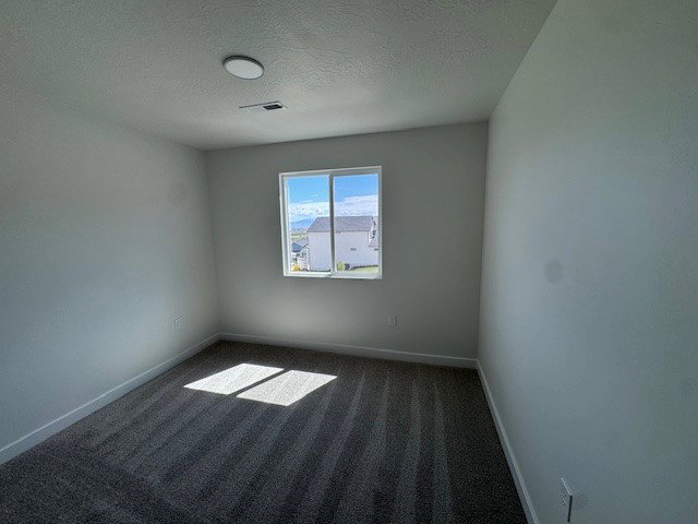 Spare room featuring dark colored carpet and a textured ceiling