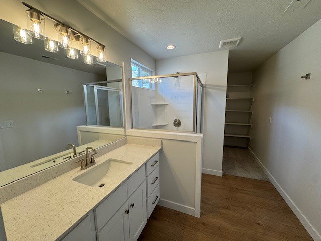 Bathroom featuring vanity, a textured ceiling, a shower stall, a walk in closet, and dark wood finished floors