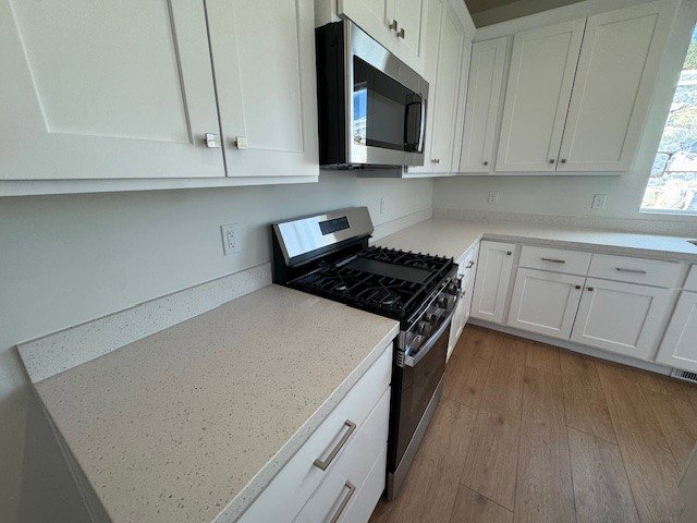 Kitchen featuring stainless steel appliances, white cabinets, dark wood-style floors, and light stone countertops
