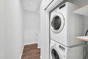 Laundry area with stacked washing machine and dryer and dark wood-style flooring