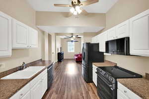 Kitchen with black appliances, white cabinetry, dark countertops, and dark wood-type flooring