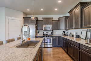 Kitchen featuring dark wood finish cabinets, stainless steel appliances, hanging light fixtures, light wood-style flooring, and a kitchen bar