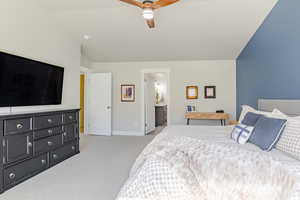 Bedroom featuring light carpet, vaulted ceiling, ceiling fan, and ensuite bathroom