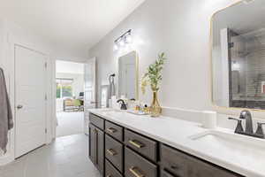 Full bathroom featuring double vanity, tiled shower, and light tile patterned floors