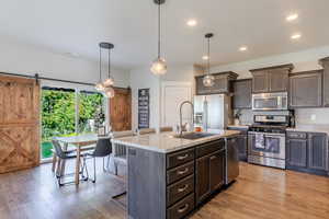 Kitchen with a barn door, stainless steel appliances, pendant lighting, dark wood finish cabinets, and light stone counters
