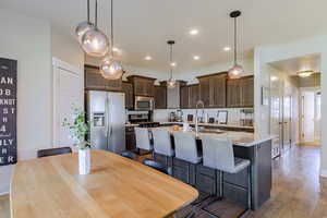 Kitchen with dark wood finish cabinets, stainless steel appliances, pendant lighting, light stone countertops, and light wood finished floors