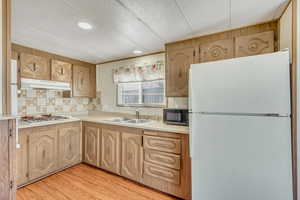 Kitchen with freestanding refrigerator, light countertops, light wood finish cabinets, light wood-style floors, and black microwave